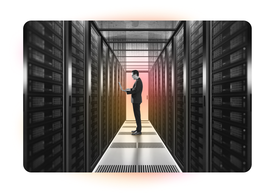 A man with long hair and a beard, wearing a denim jacket, sits at a desk and looks at the camera, with other people working in the background and abstract pink and orange lines overlaid on the image.